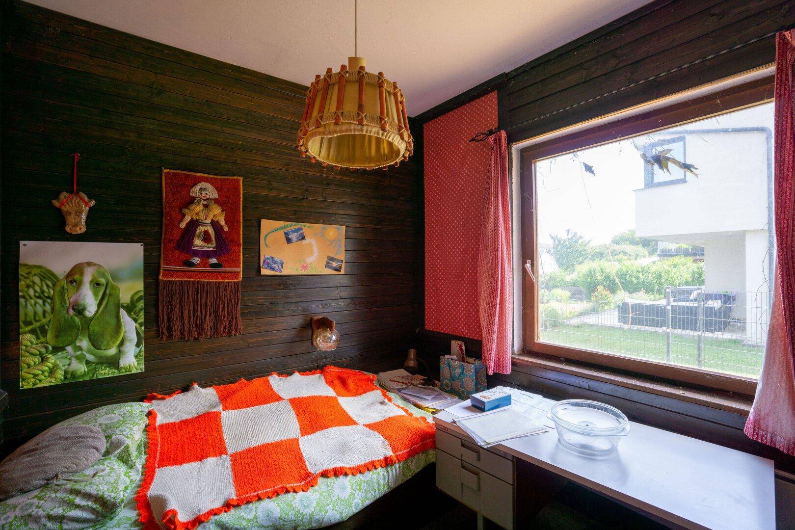 Schlafzimmer mit Holzvertäfelung, Einzelbett und Blick in den Garten.