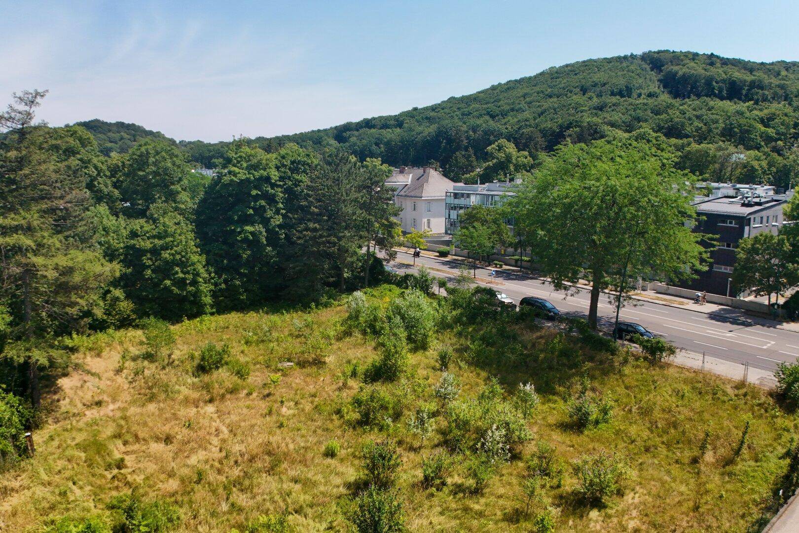 Aussicht auf ein großes, grünes Grundstück mit einer Straße, Gebäuden und bewaldeten Bergen in der Ferne.