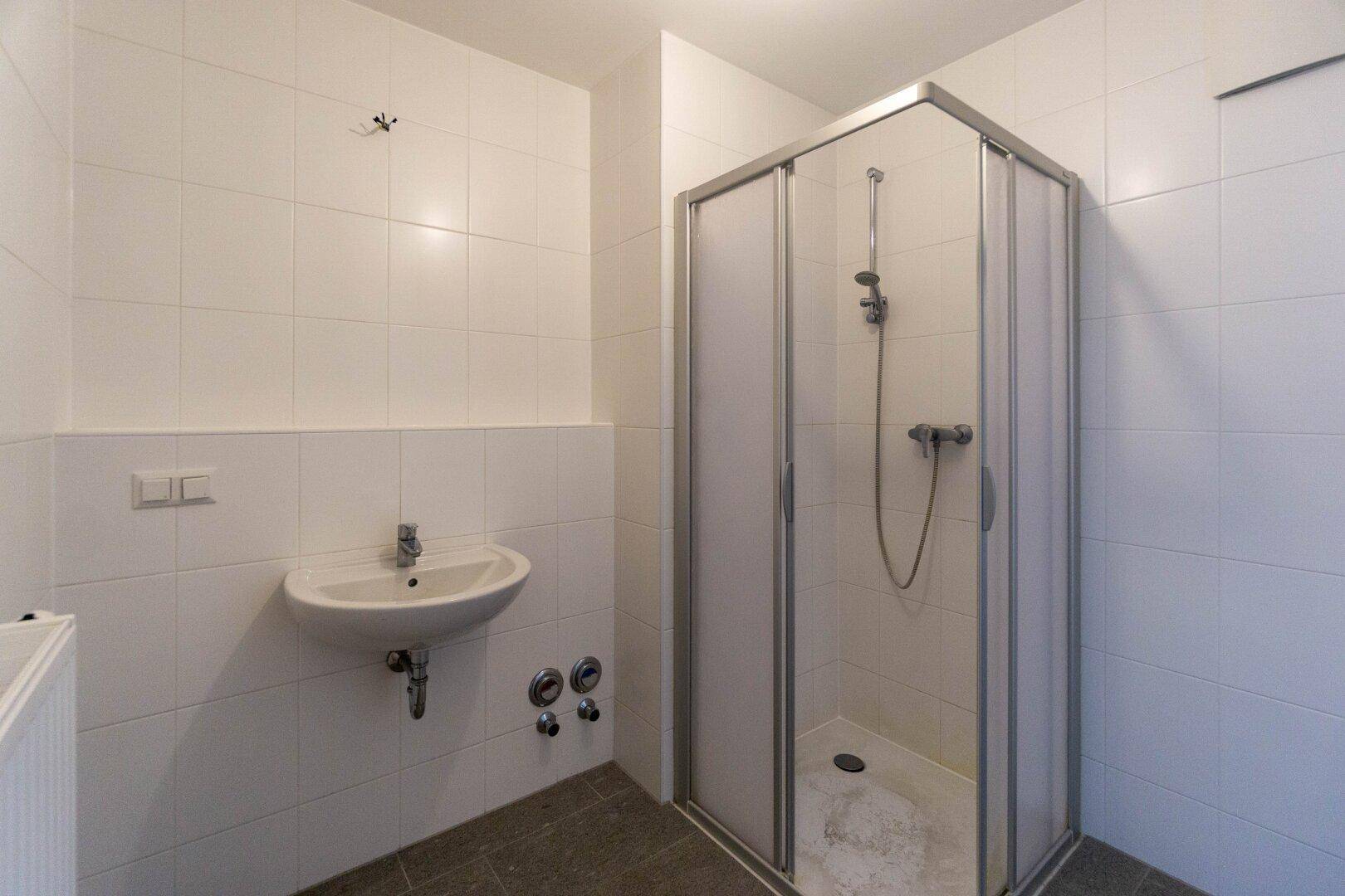 Funktionales Badezimmer mit Duschkabine, Waschbecken und weißen Wandfliesen.