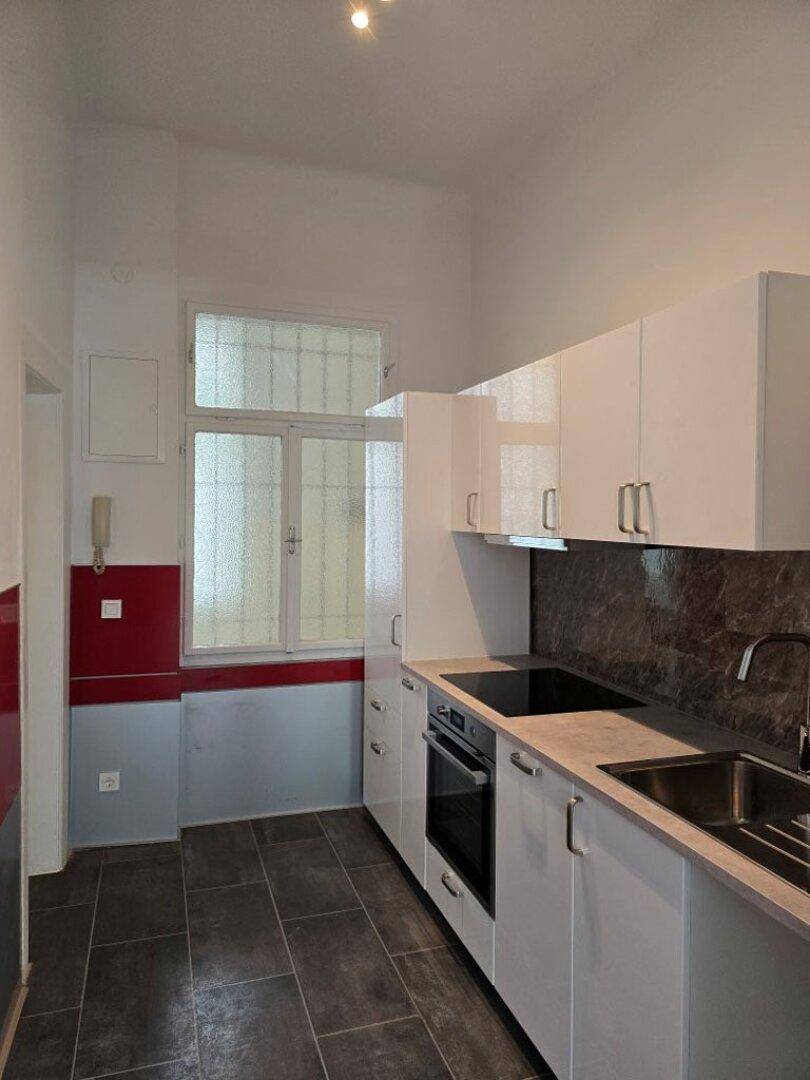Moderne Küche mit weißen Schränken, dunkler Arbeitsplatte, Induktionskochfeld und Fenster.