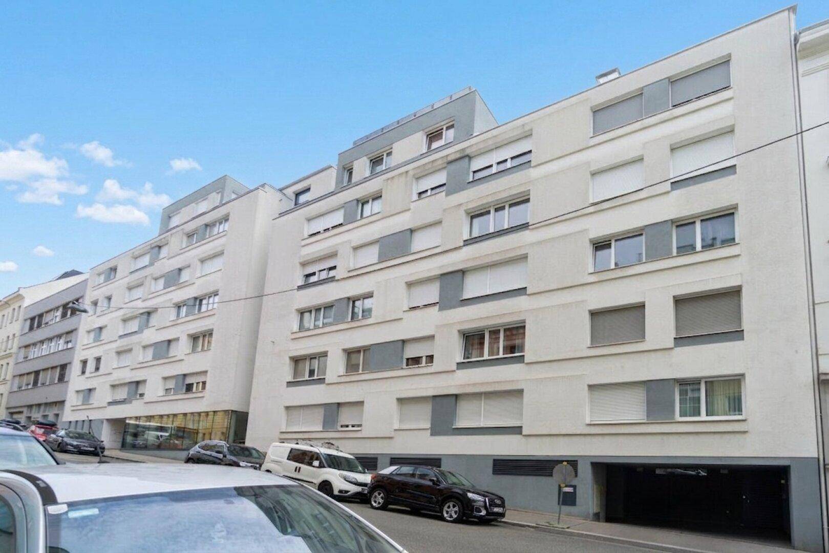 Moderne Wohnhausfassade mit zahlreichen Fenstern und Rollläden in einer städtischen Umgebung.