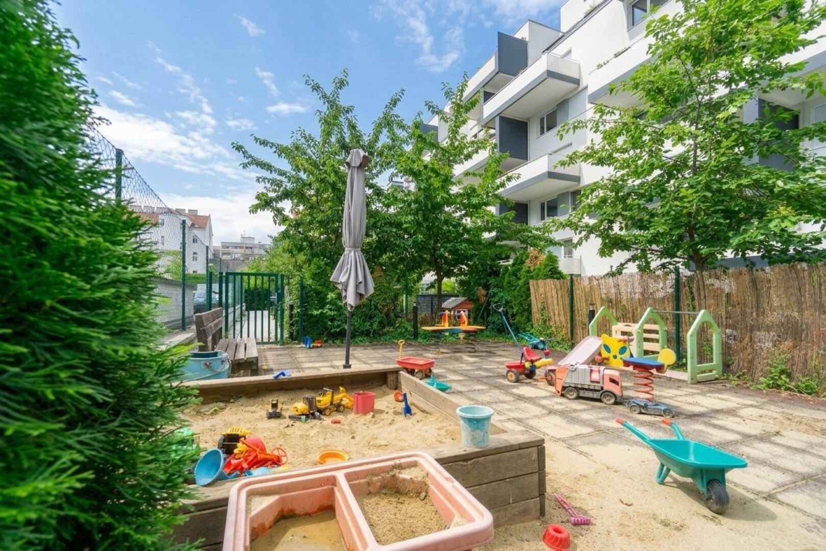 Kinderspielplatz im Freien mit Sandkasten, Schaukeln und verschiedenen Spielgeräten.
