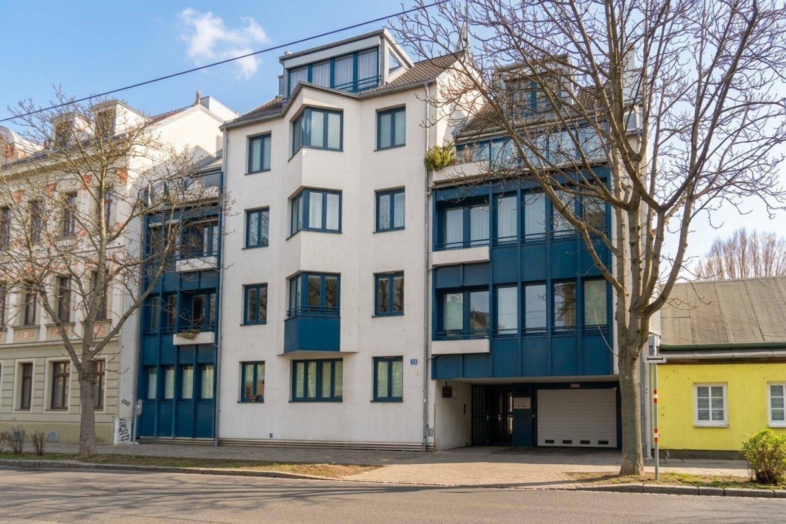 Modernes Mehrfamilienhaus mit weißer Fassade, blauen Akzenten, Erkerfenstern und integrierter Garage in urbaner Umgebung.