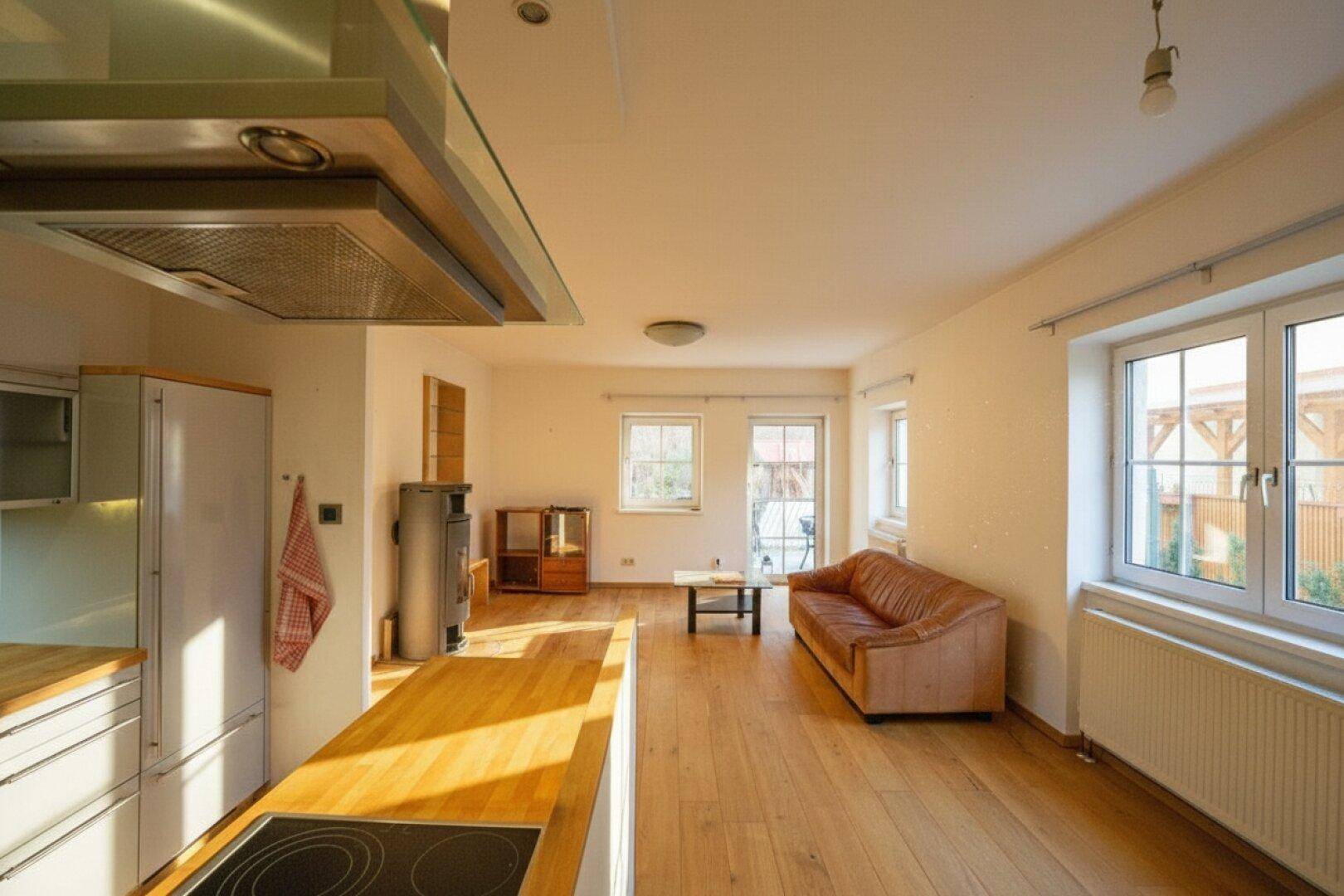 Helles, offenes Wohn-Esszimmer mit Holzboden, integrierter Küche und Zugang zum Außenbereich.
