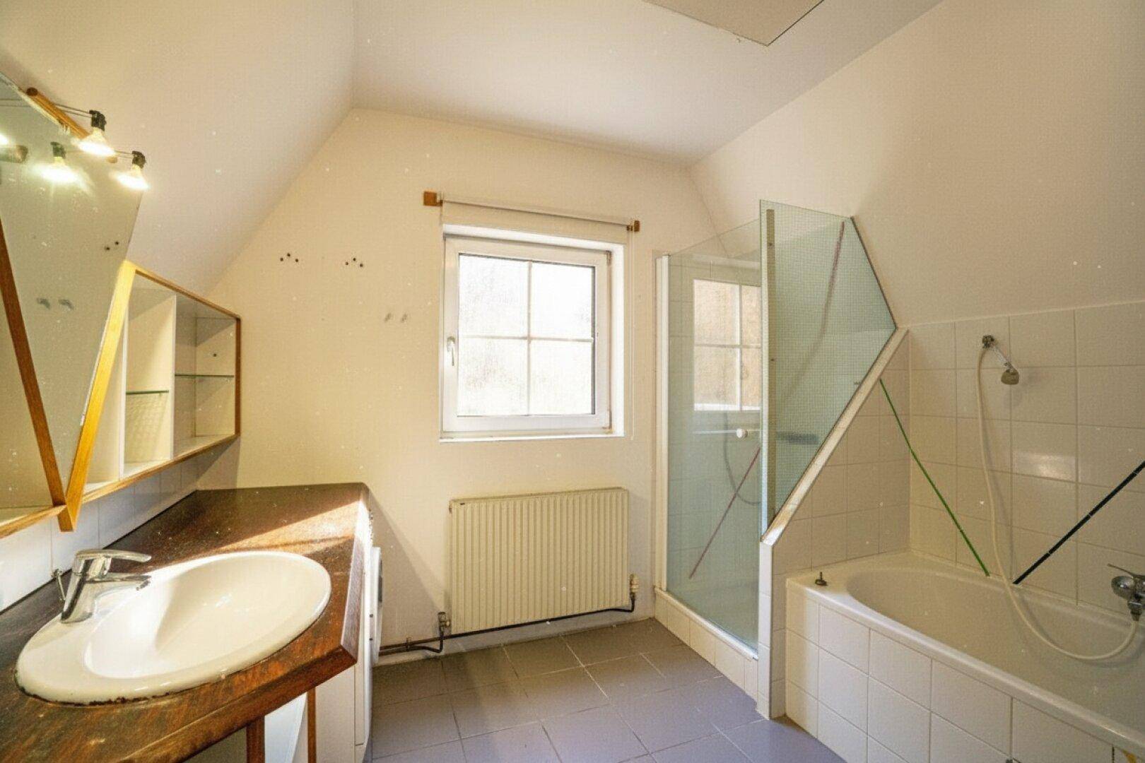 Helles Badezimmer mit Dachschräge, Badewanne, Dusche und Fenster.