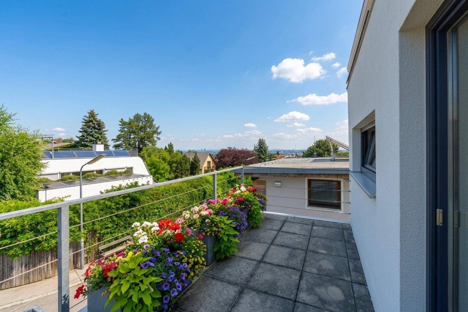 Blumengeschmückter Balkon mit weitem Blick über die umliegende Wohngegend an einem sonnigen Tag.