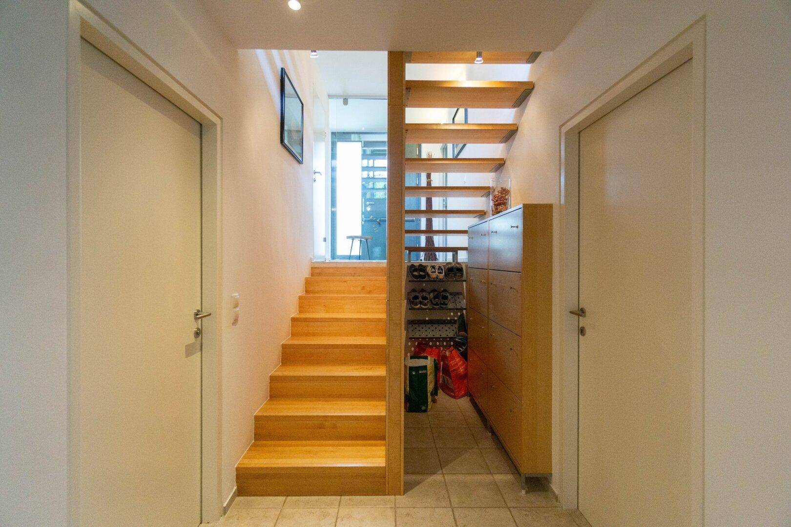 Heller Flur mit Holztreppe und praktischem Schuhschrank, der zu den oberen Etagen führt.