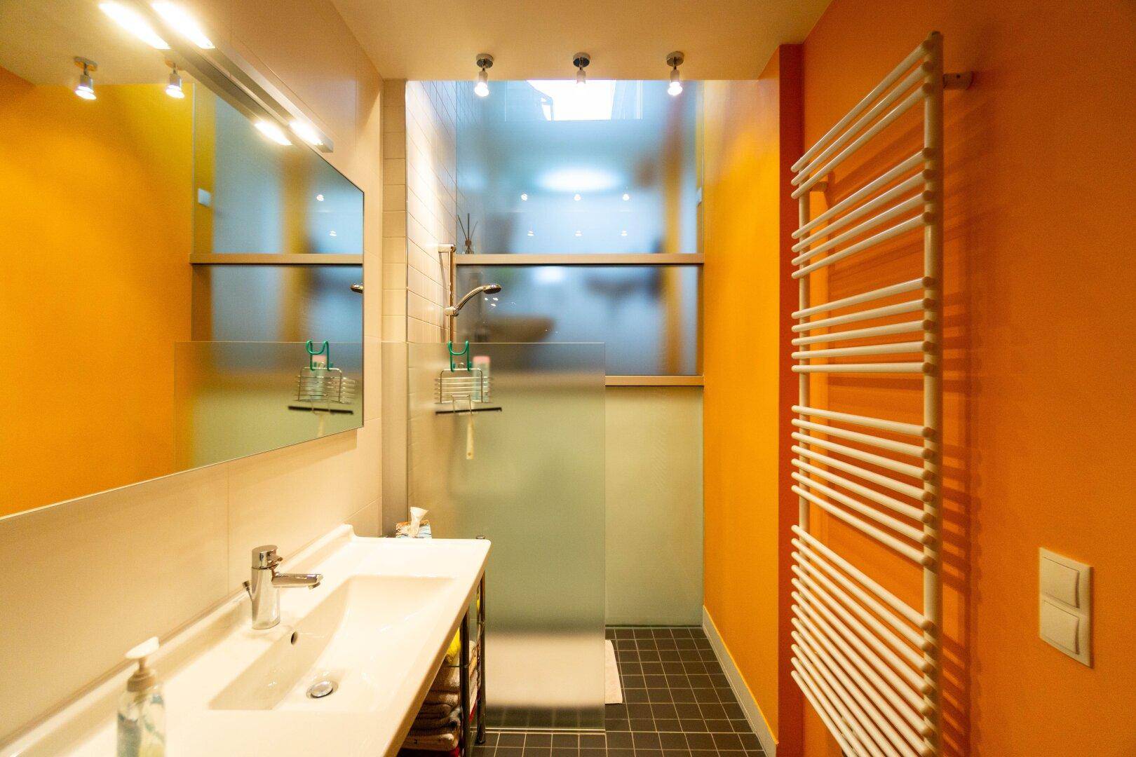 Modernes Badezimmer mit leuchtend orangefarbenen Wänden, Dusche und beheiztem Handtuchhalter.