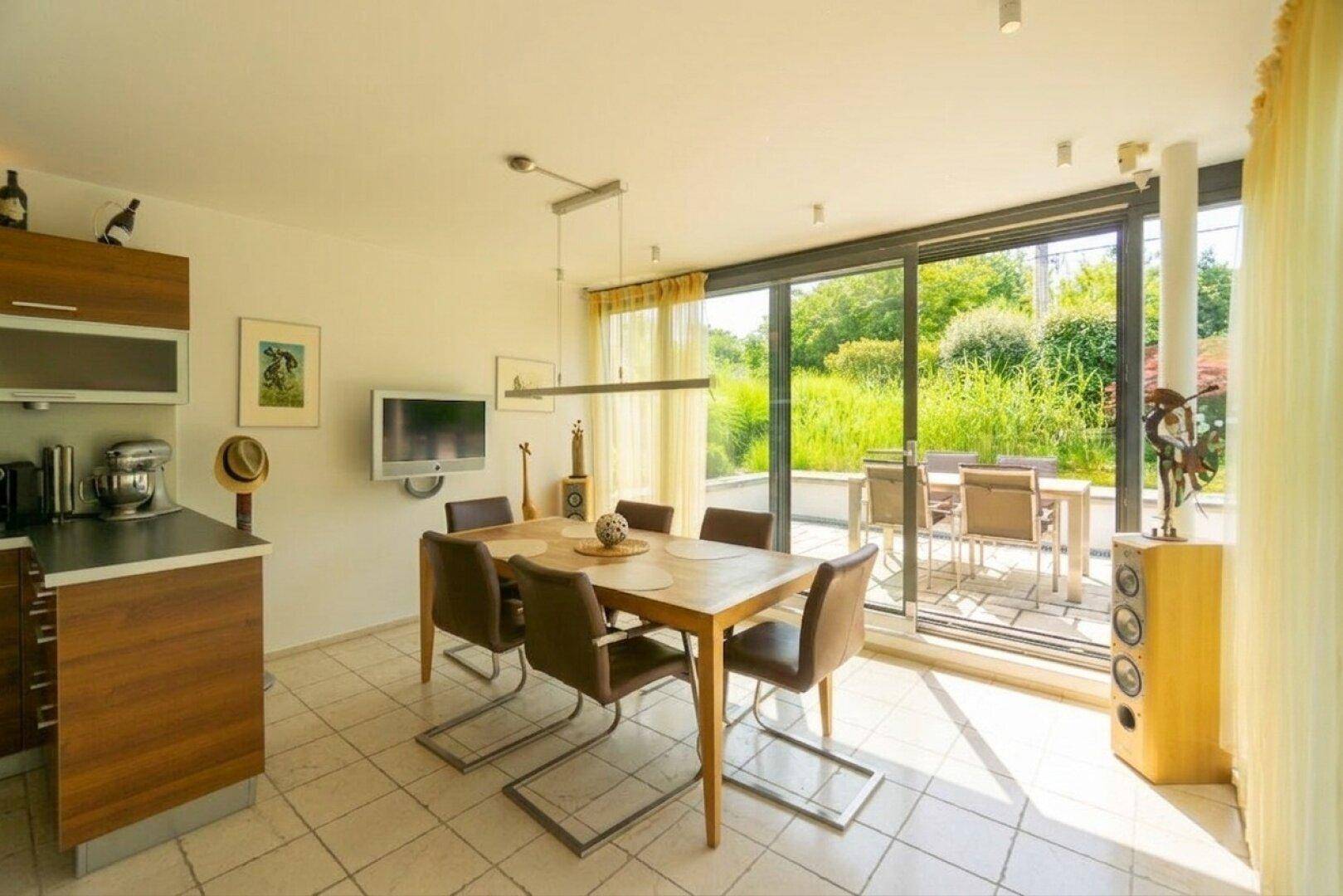 Heller Wohn-Essbereich mit Fliesenboden, Holztisch und Zugang zur Terrasse mit Gartenblick.