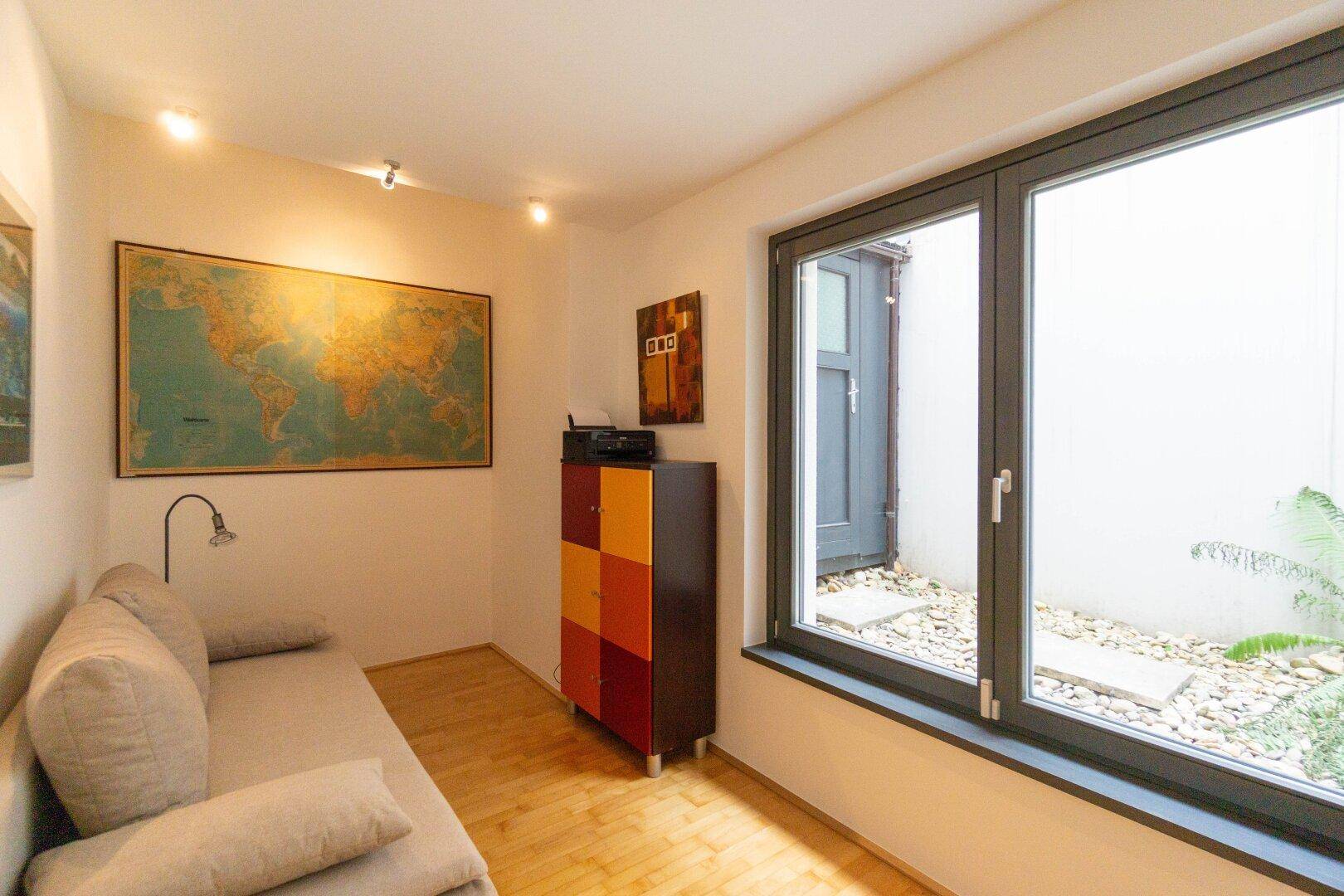 Gemütlicher Raum mit Holzboden, Sofa und Blick auf einen kleinen Innenhof mit Kies.