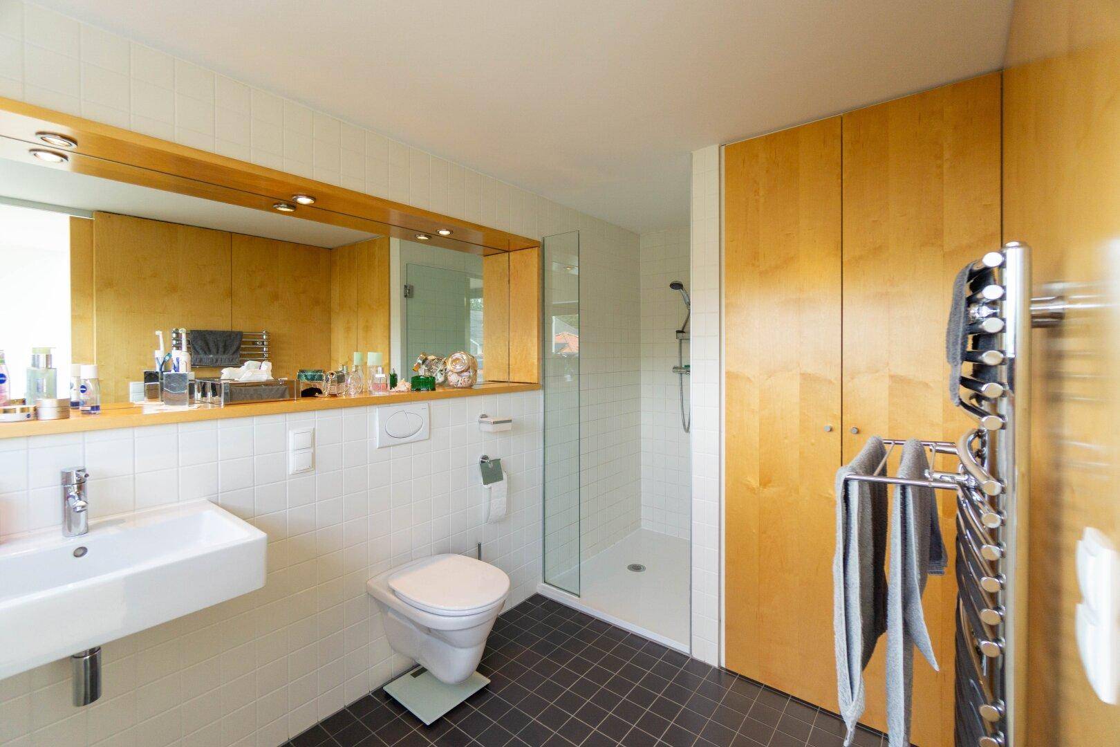 Modernes Badezimmer mit Dusche, wandhängendem WC, Einzelwaschbecken und Handtuchheizkörper.