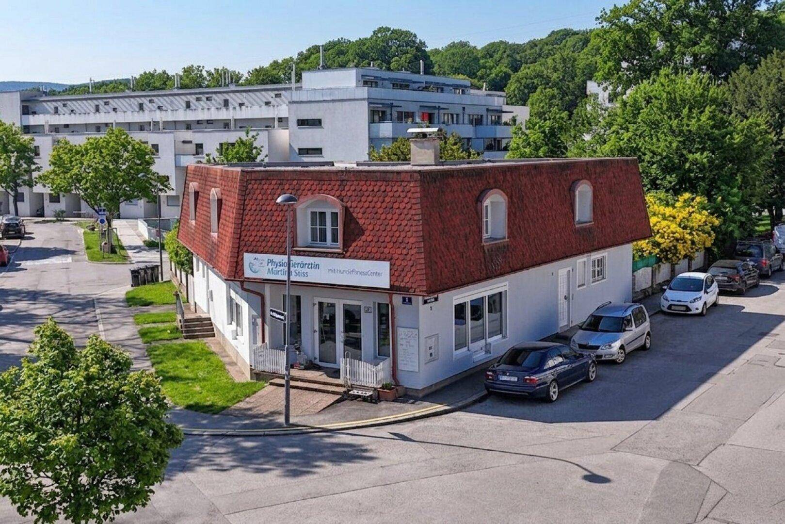 Gebäude an einer Straßenecke mit Mansarddach und umliegenden Parkplätzen.