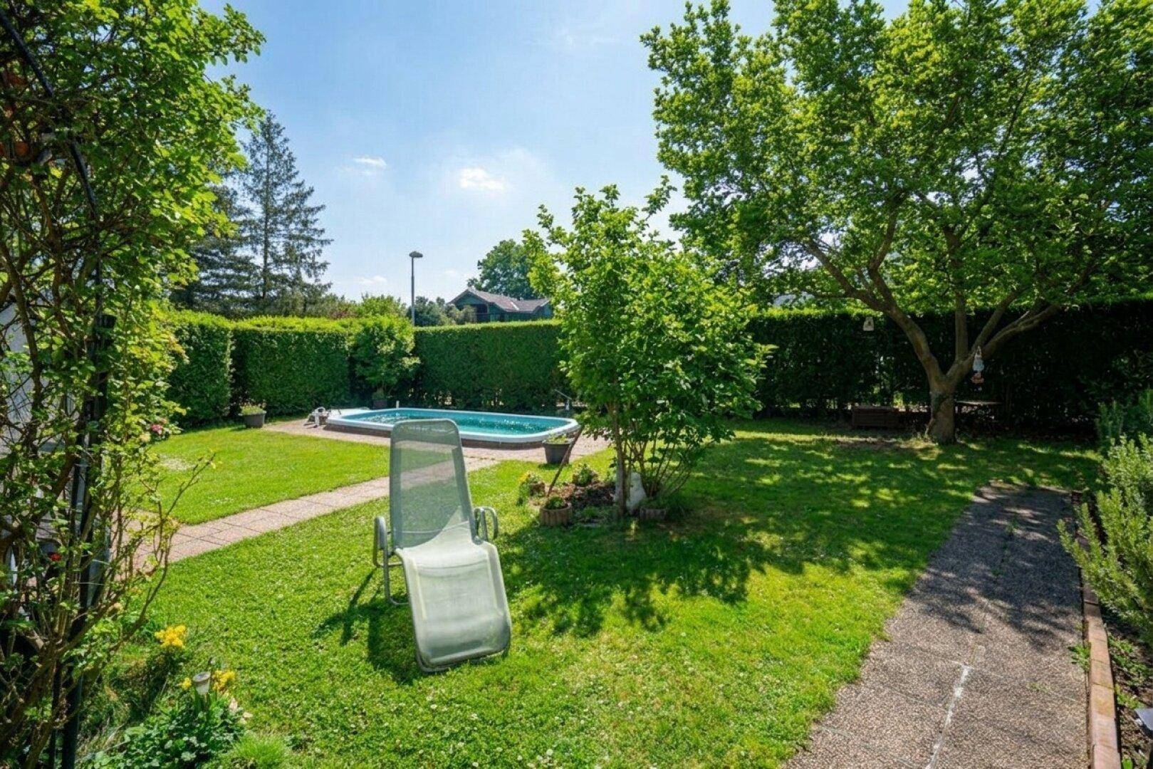 Sonniger Gartenbereich mit Swimmingpool, Liegestuhl und üppiger Vegetation.