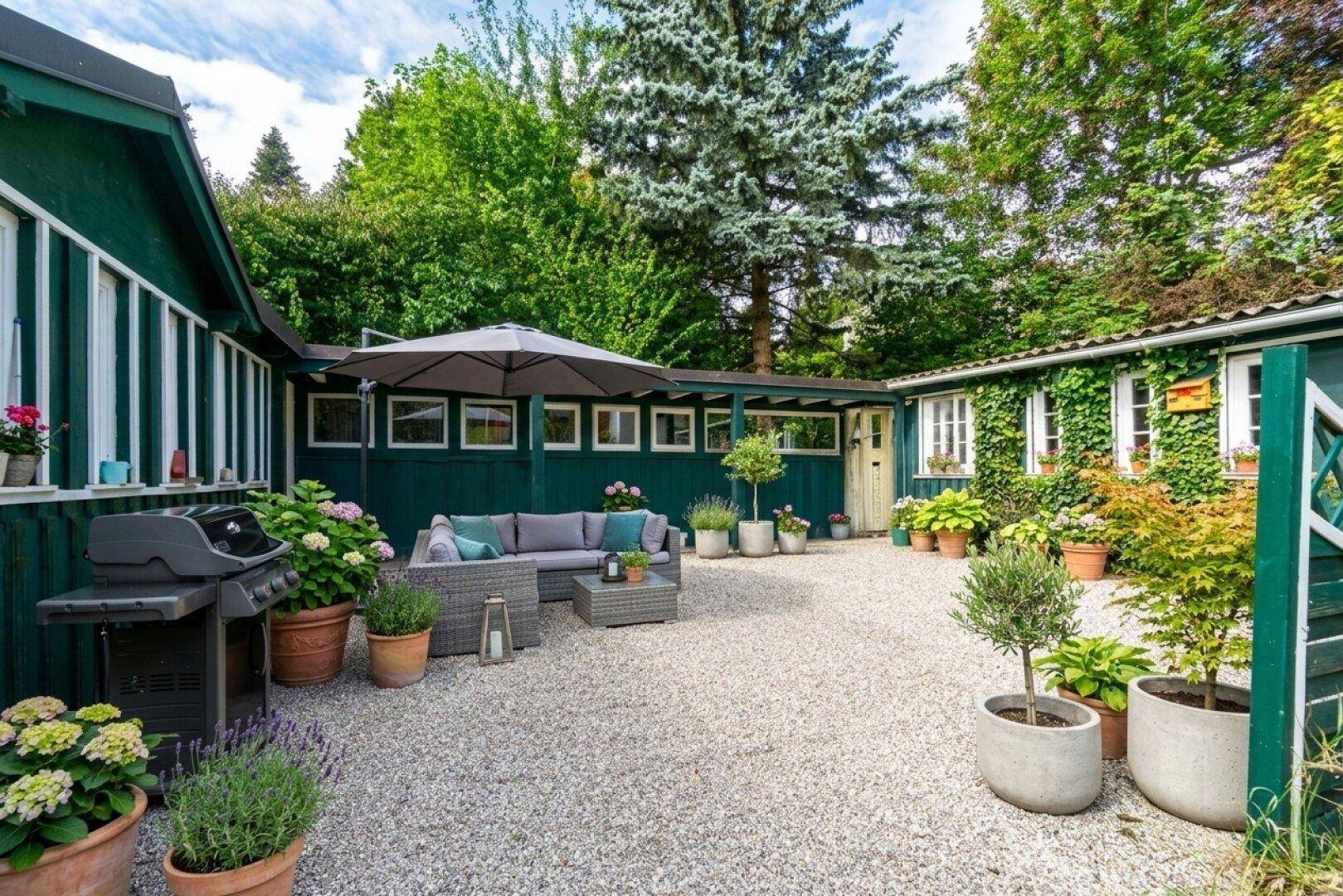 Gemütlicher Innenhof mit Lounge-Möbeln, Sonnenschirm und vielen Topfpflanzen.
