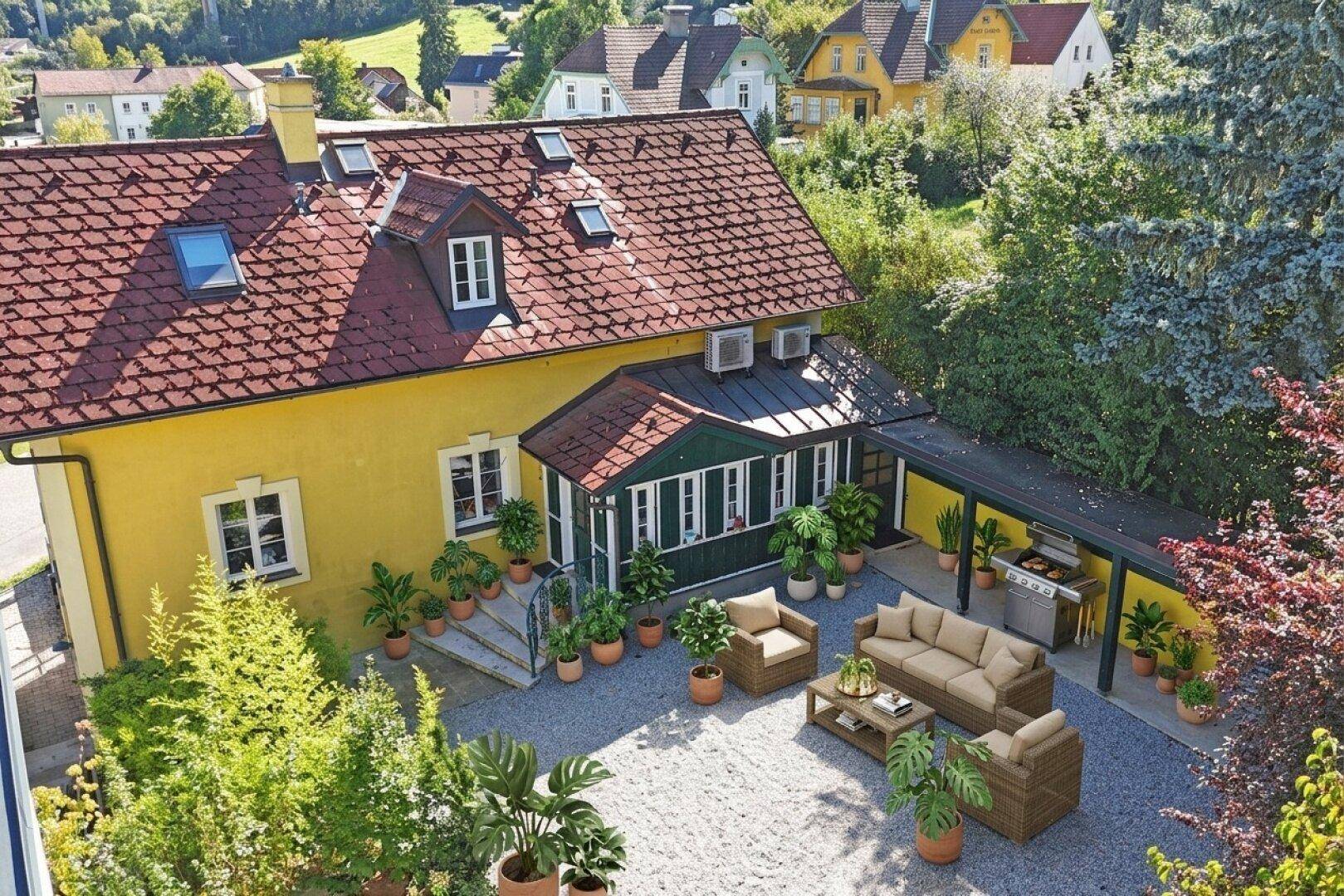 Vogelperspektive des Hauses mit gelber Fassade, rotem Dach und gemütlicher Terrasse mit Grillbereich.
