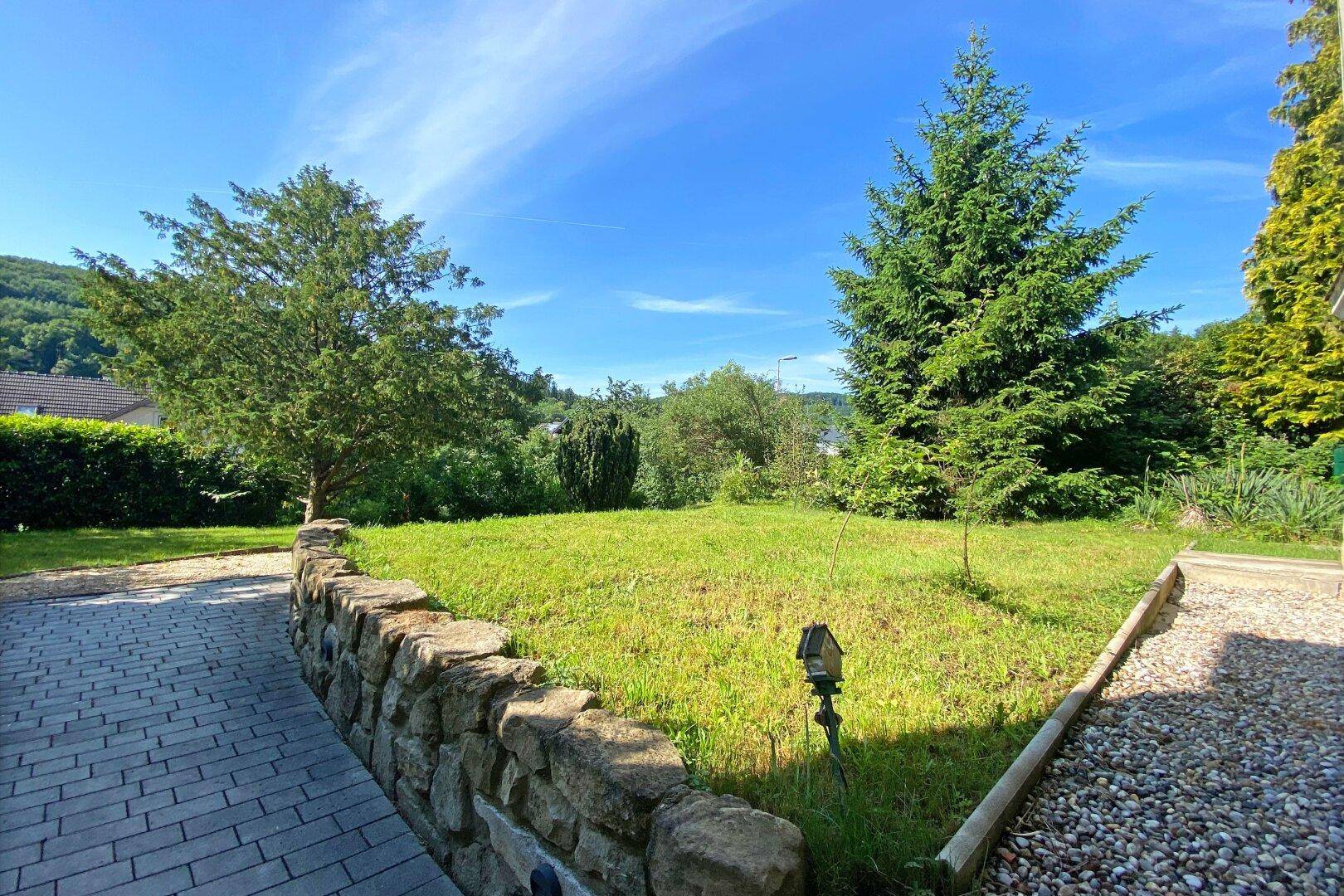 Idyllischer Gartenbereich mit Steinmauer und weitem Blick über die grüne Hügellandschaft.