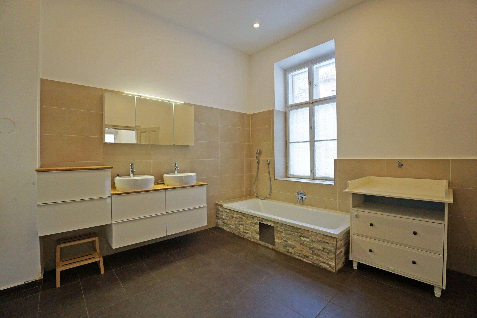 Modernes Badezimmer mit Doppelwaschbecken, Badewanne und großem Fenster für Tageslicht.