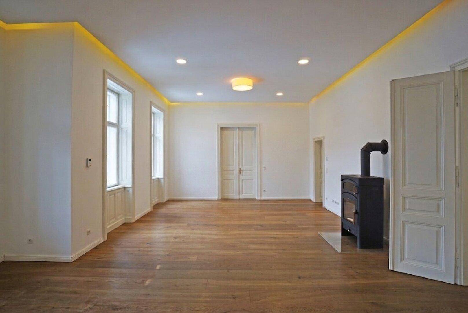 Großzügiges Wohnzimmer mit Holzboden, Kaminofen und indirekter Beleuchtung, bereit zur Einrichtung.