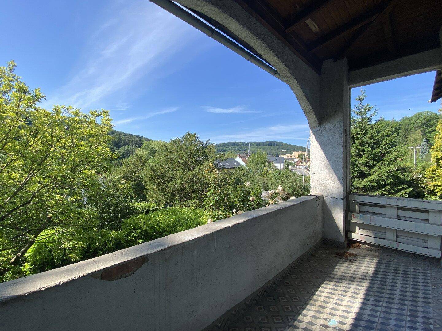 Überdachter Balkon mit Fliesenboden und weitem Blick über die grüne Landschaft und das Tal.