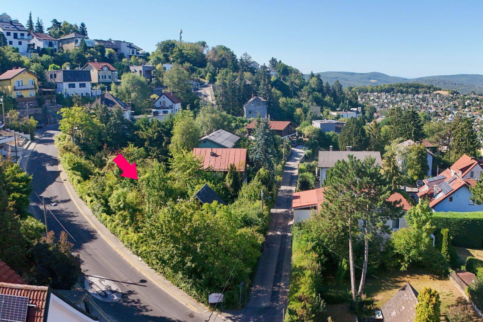 Luftaufnahme einer grünen Wohngegend am Hang mit vielen Häusern und weitem Blick auf die Landschaft.
