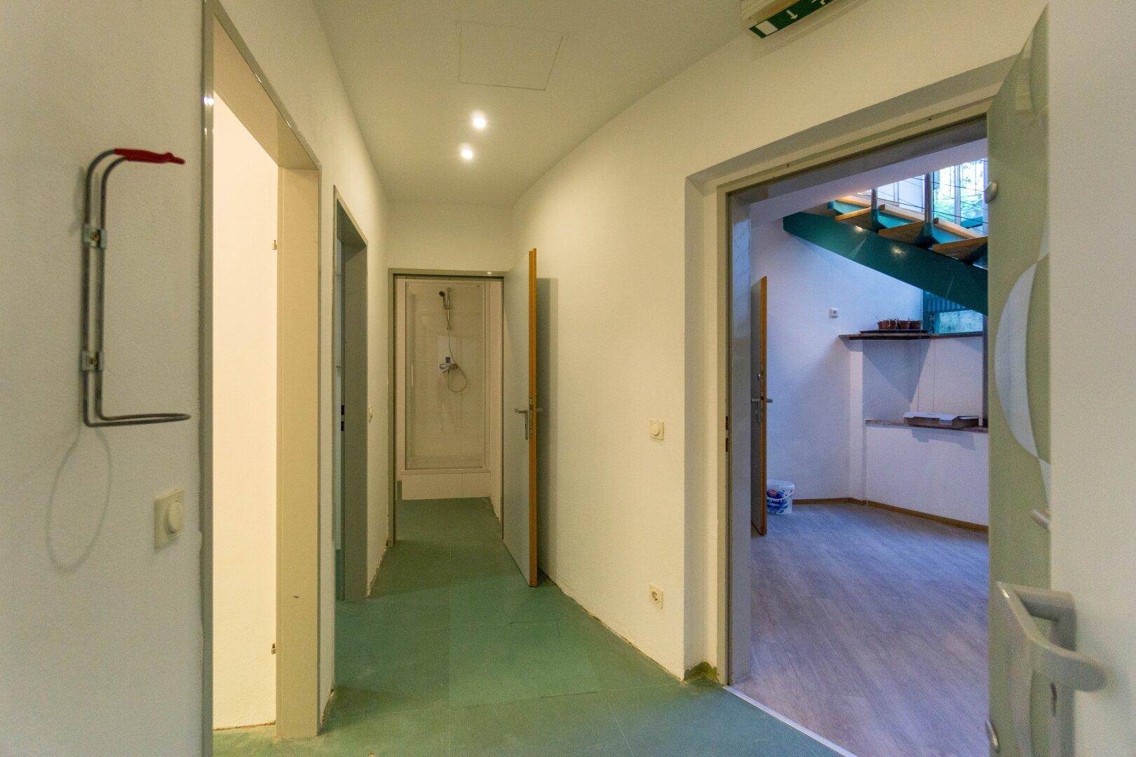 Langer Flur mit hellem Boden, weißen Wänden und Türen, der zu weiteren Räumen führt.