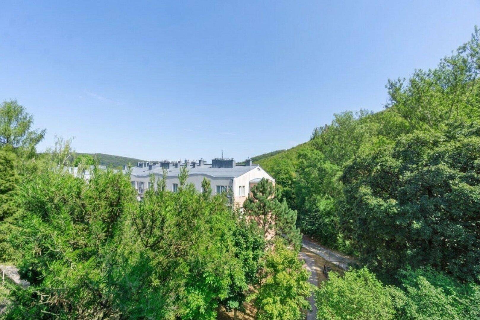 Panoramablick auf eine Wohnsiedlung umgeben von dichtem Grün und bewaldeten Hügeln.