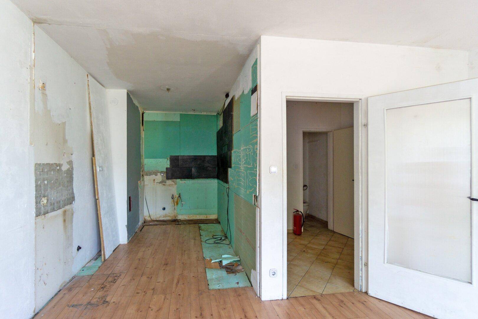 Leerer Raum mit Laminatboden und vorbereiteter Küchennische, die auf eine neue Einrichtung wartet.