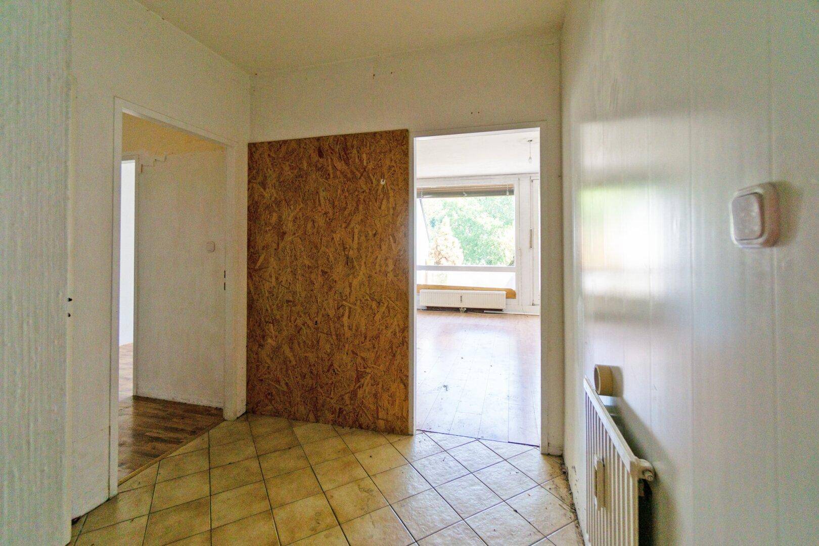 Flur mit Fliesenboden und Zugang zu weiteren Räumen, die auf Renovierung warten.
