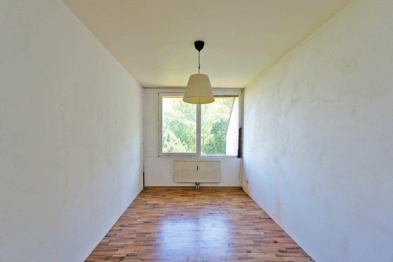 Helles, leeres Zimmer mit Laminatboden und Fenster, das auf eine neue Gestaltung wartet.