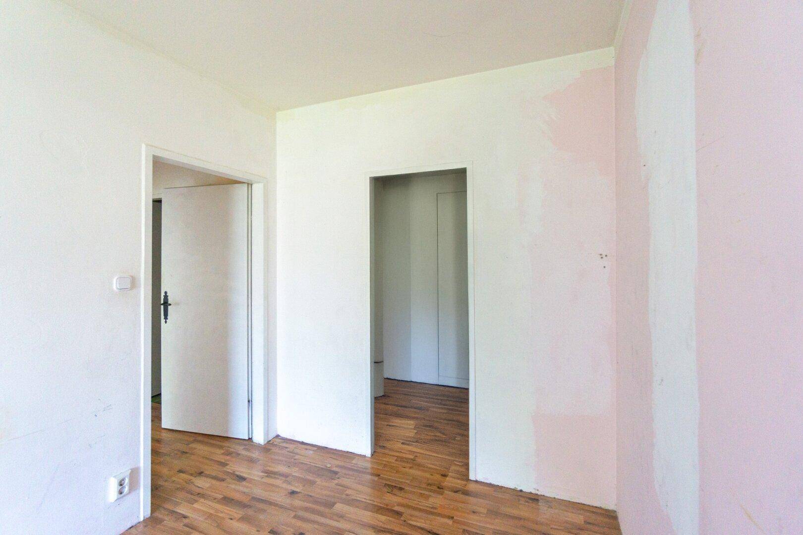 Flur mit Laminatboden und Zugang zu weiteren Räumen, die auf Renovierung warten.