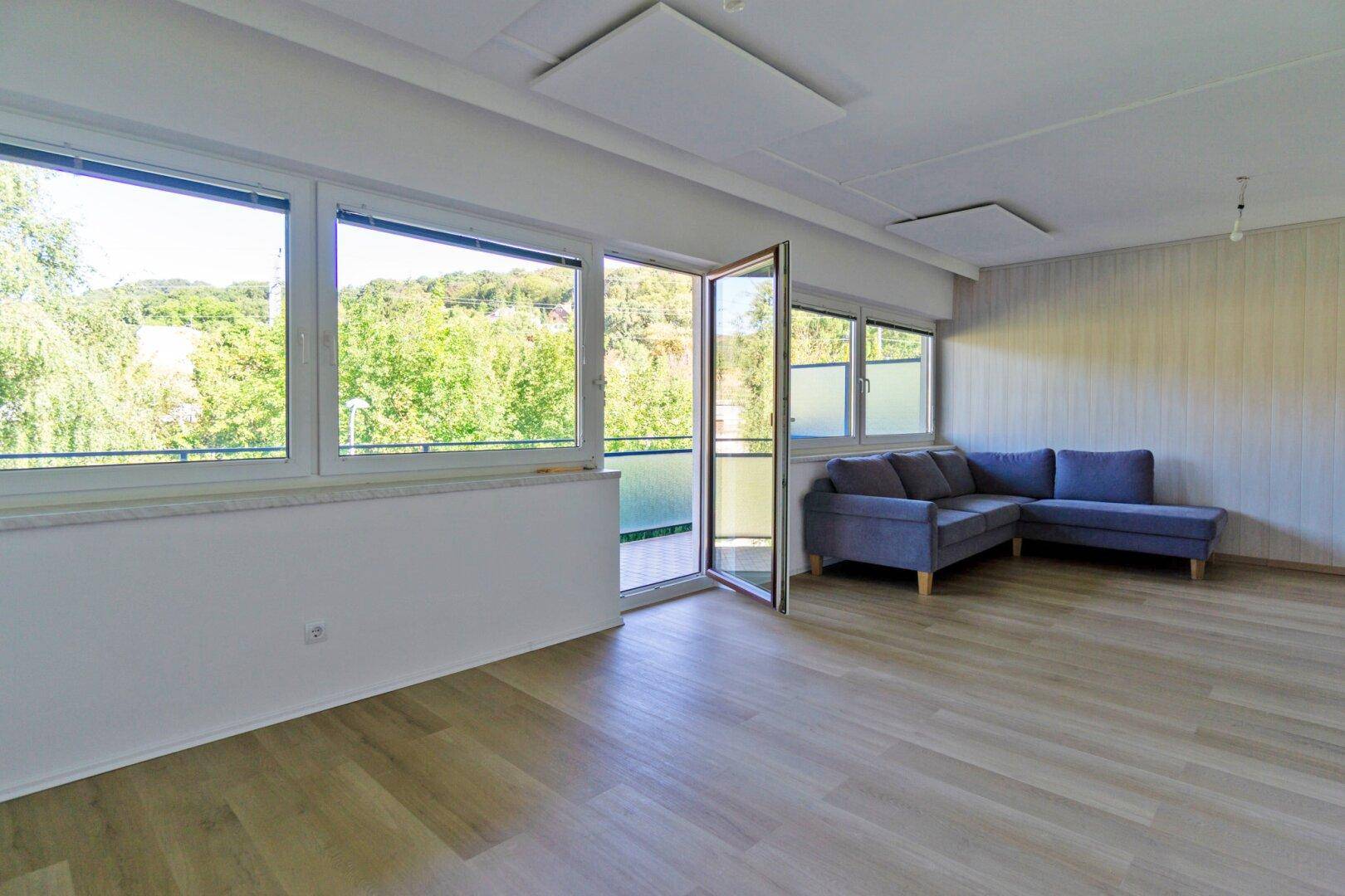 Geräumiges Wohnzimmer mit großzügigen Fenstern, Holzboden und einem bequemen Sofa.