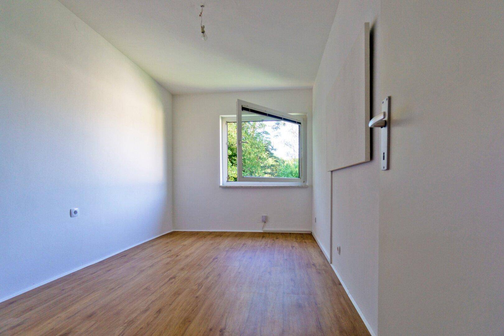 Helles, leeres Zimmer mit Laminatboden und einem Fenster, das viel Tageslicht bietet.