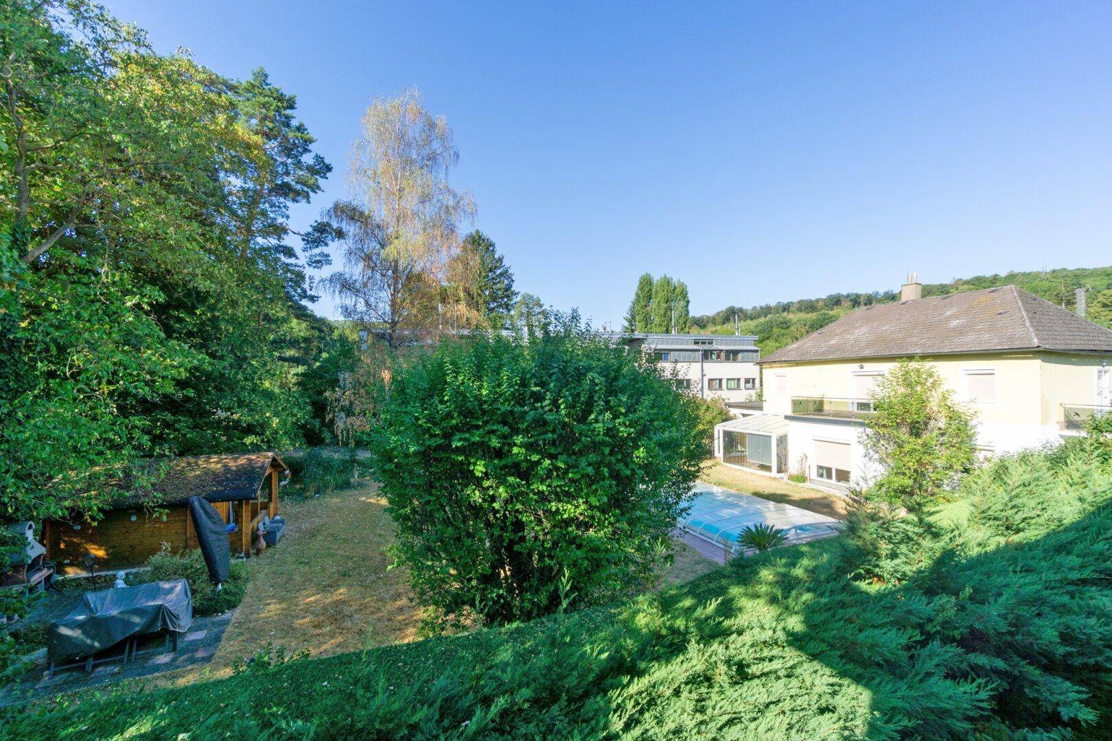 Weitläufige Außenansicht der Umgebung mit viel Grün, einem Pool und angrenzenden Gebäuden.