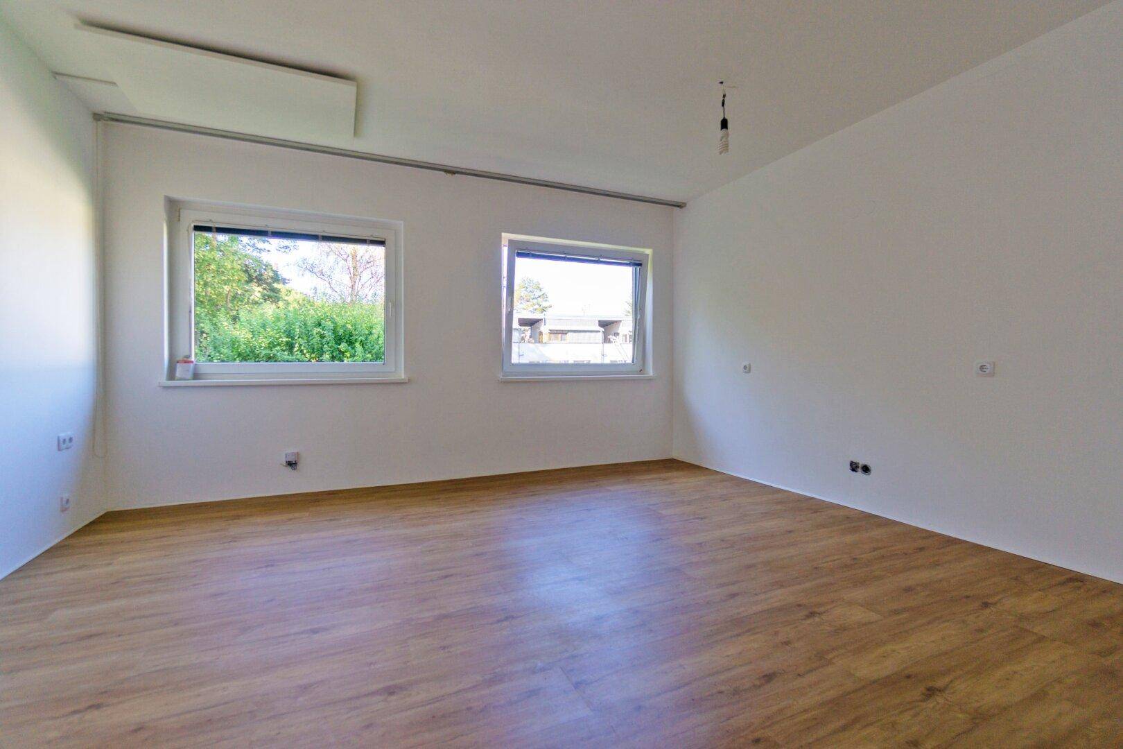 Geräumiges, helles Zimmer mit zwei Fenstern und ansprechendem Laminatboden.