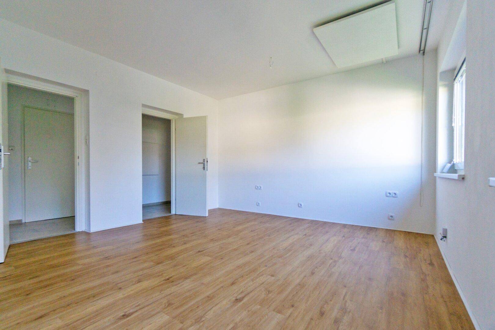 Helles Zimmer mit Laminatboden und mehreren Türen, bereit zur individuellen Gestaltung.