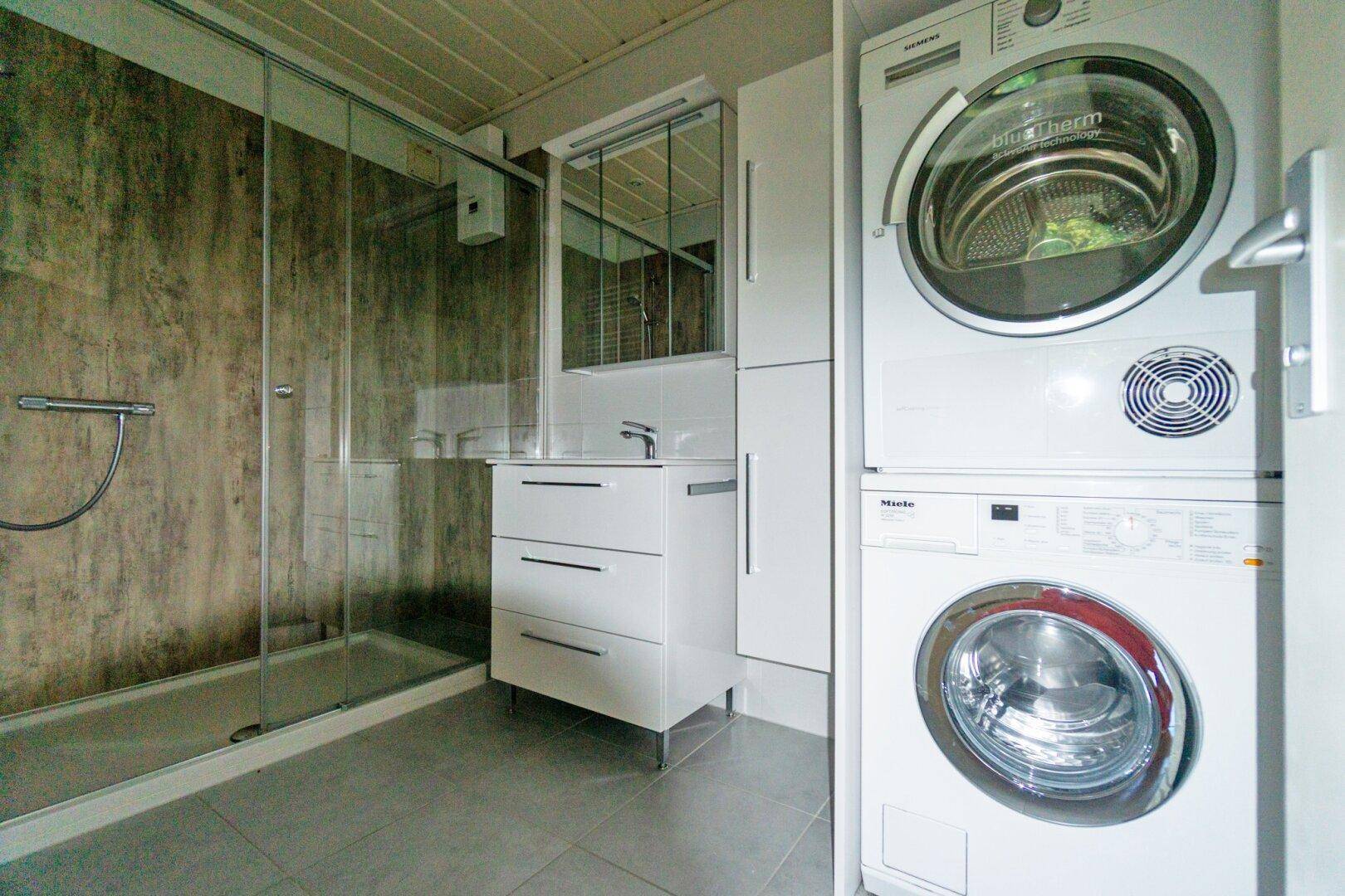 Modernes Badezimmer mit Duschkabine, Waschbecken und praktischem Waschmaschinen-Trockner-Turm.