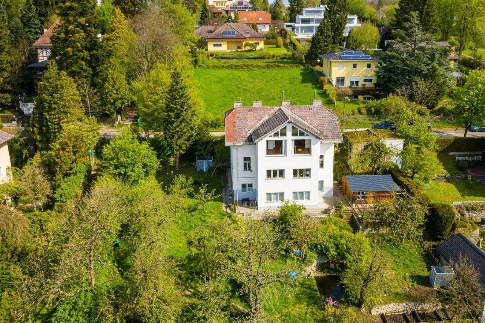 Luftaufnahme des weißen Hauses auf einem grünen Hügelgrundstück mit umliegender Natur.