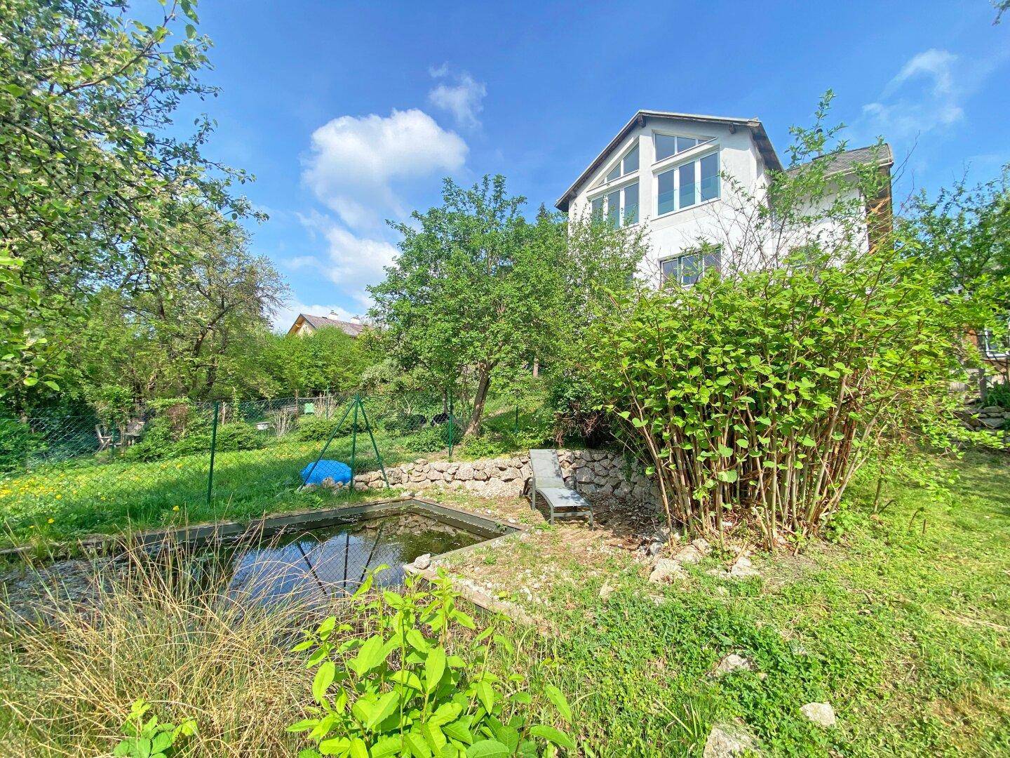 Großer Garten mit Teich, Rasenfläche und vielfältiger Bepflanzung vor dem Haus.