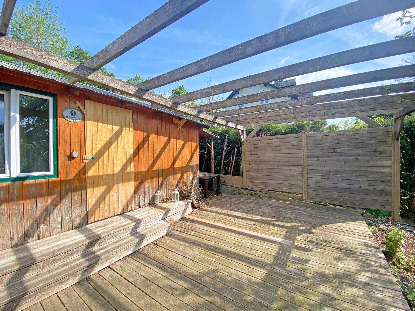 Holzterrasse mit Pergola und angrenzendem Holzschuppen, ideal für entspannte Stunden im Freien.