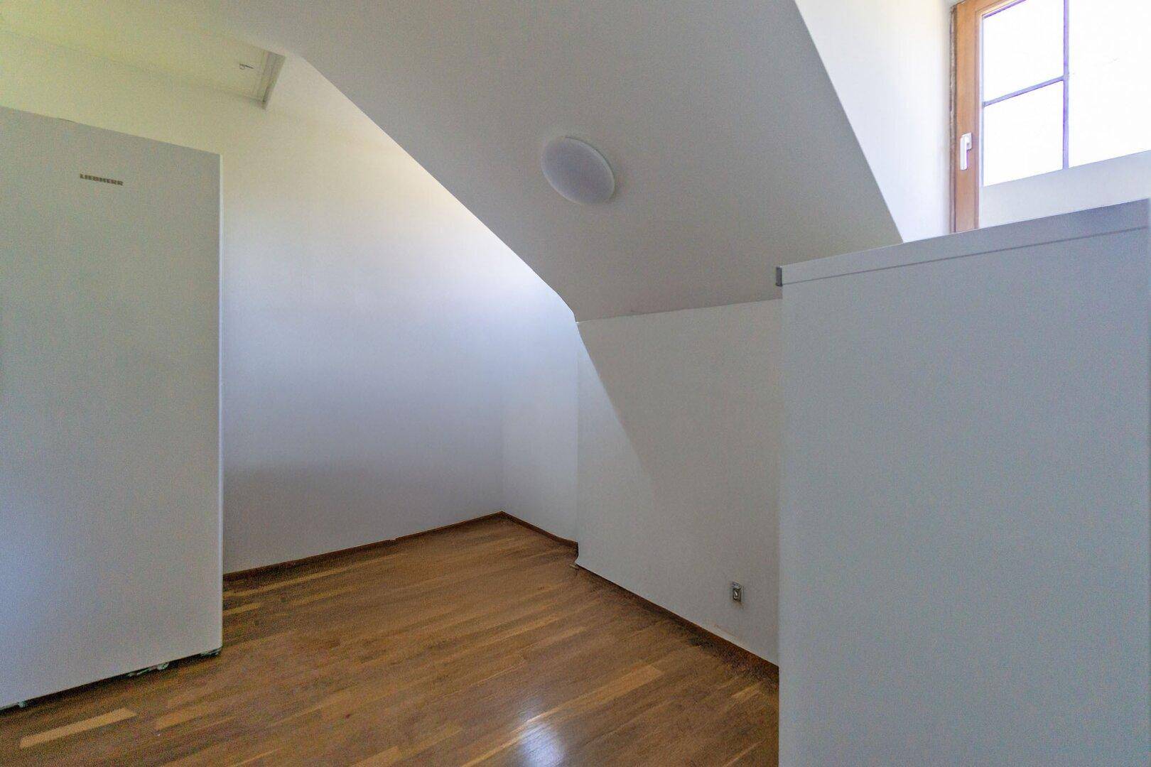 Kleiner Raum mit Dachschräge, Holzboden und einem freistehenden Kühlschrank.
