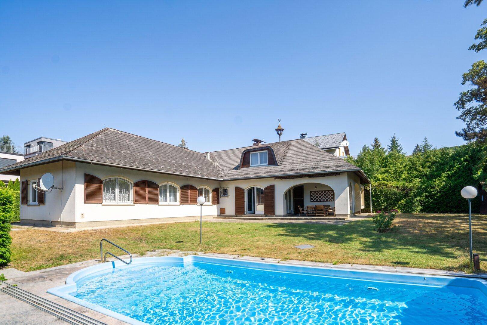 Außenansicht des Hauses mit Swimmingpool im Garten unter blauem Himmel.