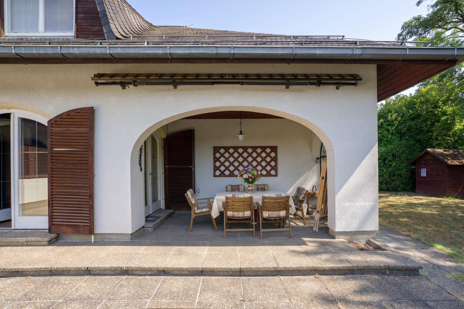 Überdachte Terrasse mit Esstisch und Stühlen, ideal für Mahlzeiten im Freien.