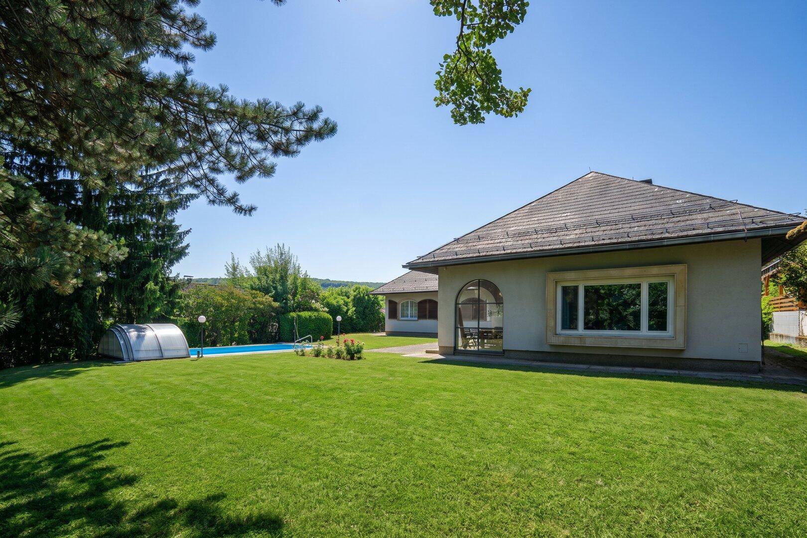 Weitläufiger Garten mit Pool und Blick auf die Hausfassade unter strahlendem Sonnenschein.