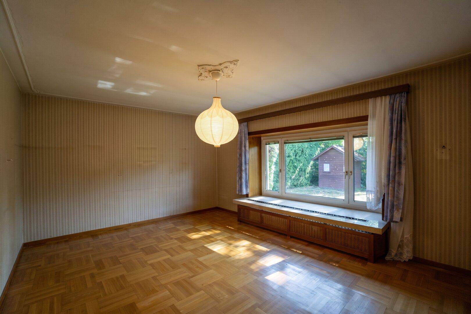 Helles Wohnzimmer mit Parkettboden, großer Fensterfront und Blick in den Garten.