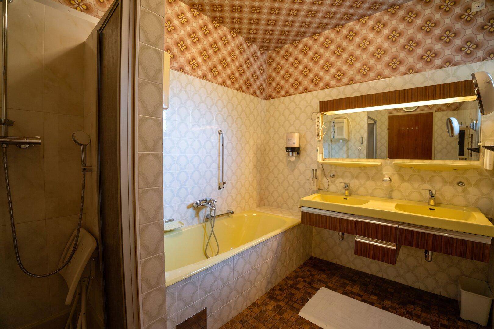 Badezimmer im Stil der 80er Jahre mit gelber Badewanne und Doppelwaschbecken.
