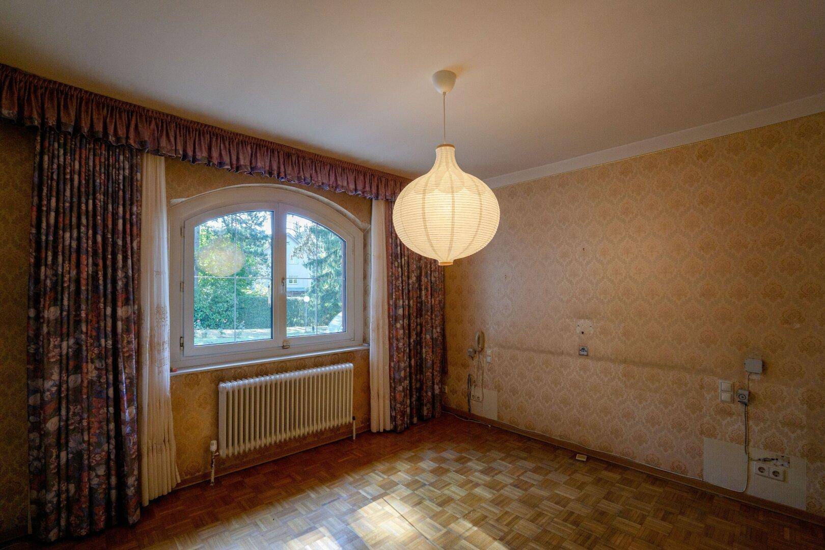 Schlafzimmer mit Parkettboden, gemusterter Tapete und großem Bogenfenster.