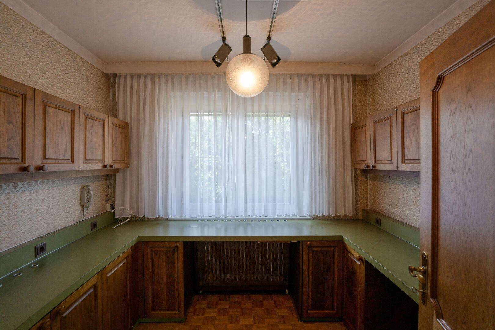 Arbeitszimmer mit Holzschränken, grüner Arbeitsplatte und großem Fenster.