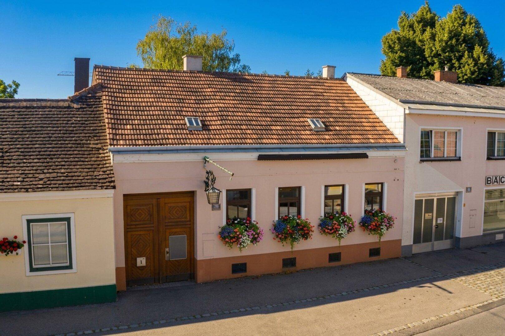 Traditionelles Gebäude mit blühenden Blumenkästen an den Fenstern und einem roten Ziegeldach.