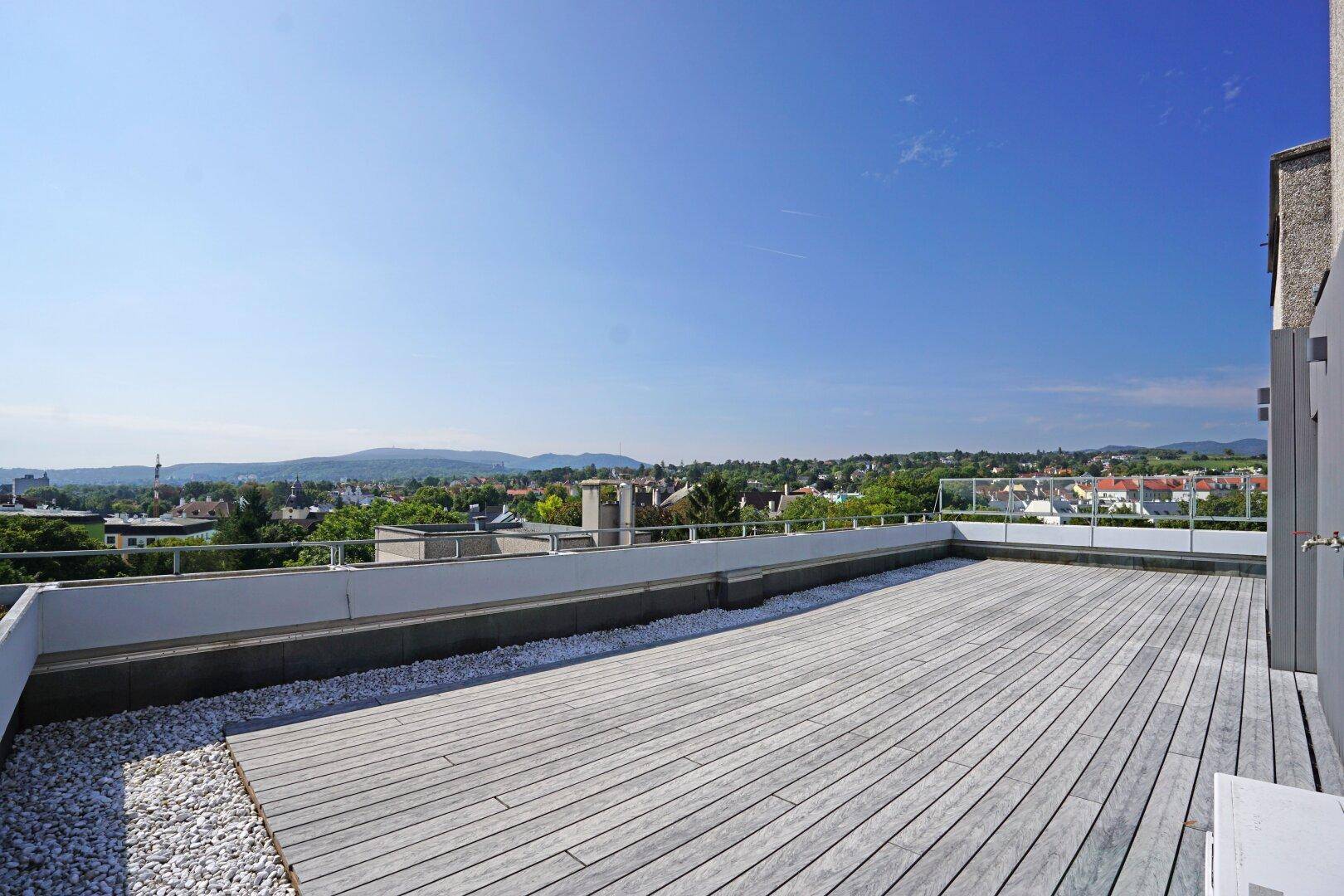Geräumige Dachterrasse mit Holzboden und weitem Blick über die Stadt und die umliegende Landschaft.