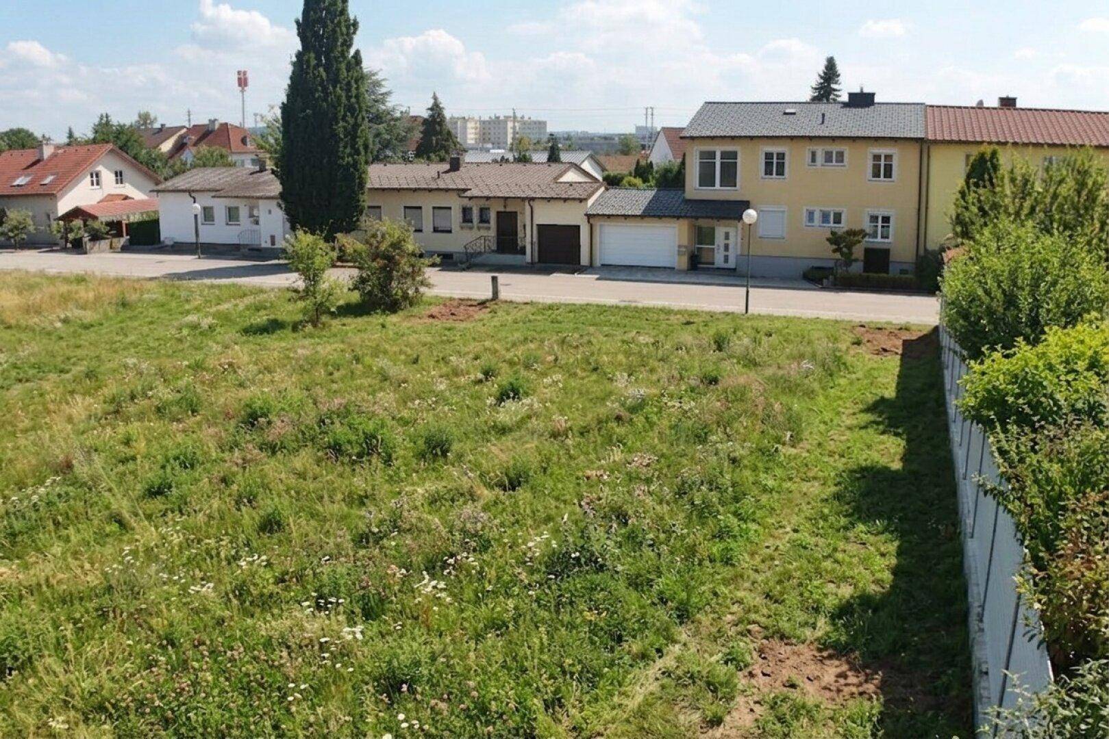 Blick über das unbebaute Grundstück auf die angrenzende Straße und die umliegenden Wohnhäuser.